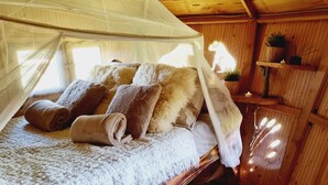 A cozy room with a canopy bed, rolled towels, and a shelf with plants. - Le Domaine de Wail Legends Resort (Wail)