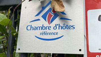 A sign with the text 'Chambre d'hôtes référence' indicating a reference room, mounted on a metal structure with surrounding greenery.