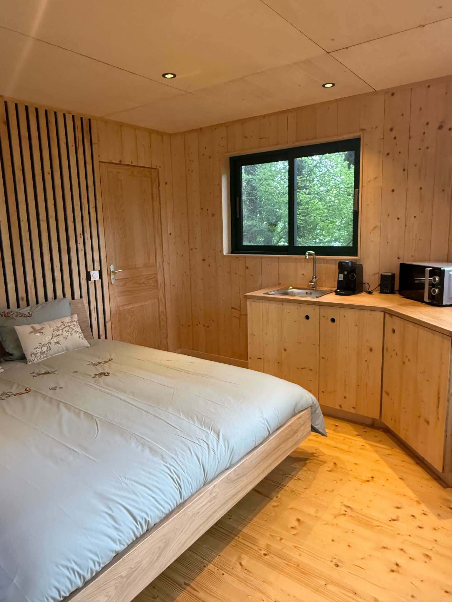 A bedroom with a bed, a window, a sink, and a coffee maker.