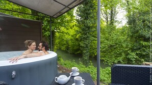 A hot tub with two people, a table with a teapot and cups, and a view of a river and greenery. - Le Domaine de Wail Legends Resort (Wail)