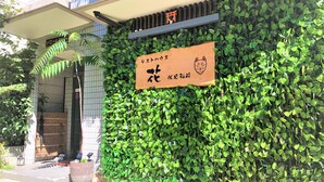 A building facade with a green leafy wall, a wooden signboard, and a small dog statue.