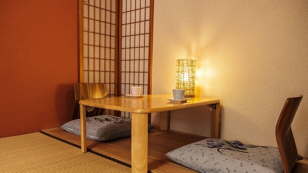 A traditional Japanese room with tatami flooring, a low wooden table, two cushions, and a shoji screen.