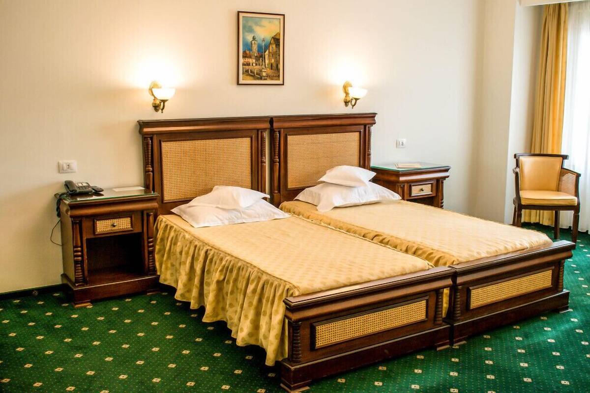 A double bed with a wooden frame and rattan headboard, two bedside tables with lamps, a chair, and a painting on the wall.