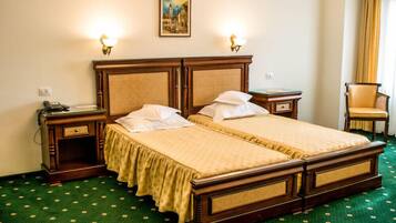 A double bed with a wooden frame and rattan headboard, two bedside tables with lamps, a chair, and a painting on the wall.