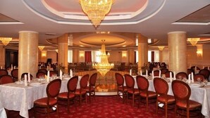 Ein formeller Speisesaal mit runden Tischen, rot gepolsterten Stühlen und einer zentralen Chandelier.