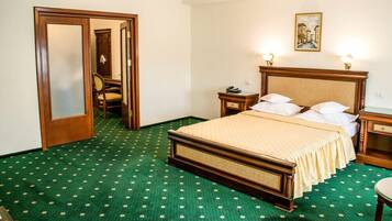 Habitación de hotel con una cama grande, un cabecero de madera, una alfombra verde estampada, un candelabro y un cuadro en la pared.