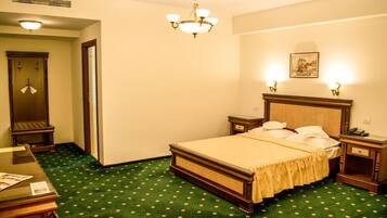 A hotel room with a bed, a desk, a chair, a dresser, a mirror, a chandelier, and a picture on the wall.