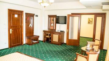 Habitación de hotel con alfombra verde, muebles de madera, escritorio, silla, cama y televisor.