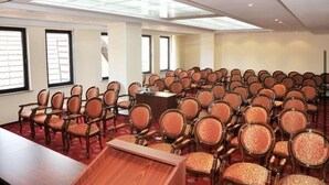 Ein Konferenzraum mit Reihen aus Holzsesseln und einem langen Tisch, großen Fenstern und einem Oberlicht.