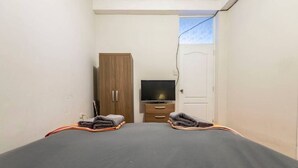 A small, single-room hotel room with a bed, a wooden wardrobe, a television, and a door.