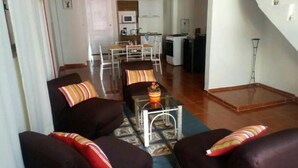 A living room with dark sofas, a coffee table, and a dining area with chairs and a table.