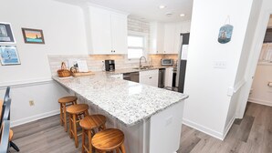 A modern kitchen with white cabinets, granite countertops, and wooden stools. - OCEANFRONT, Ocean views, screened porch, NP15-1, Pelican Dunes (Duck)
