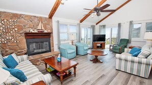 A spacious living room with a stone fireplace, multiple sofas, a television, and a ceiling fan. - OCEANFRONT, Ocean views, screened porch, NP15-1, Pelican Dunes (Duck)