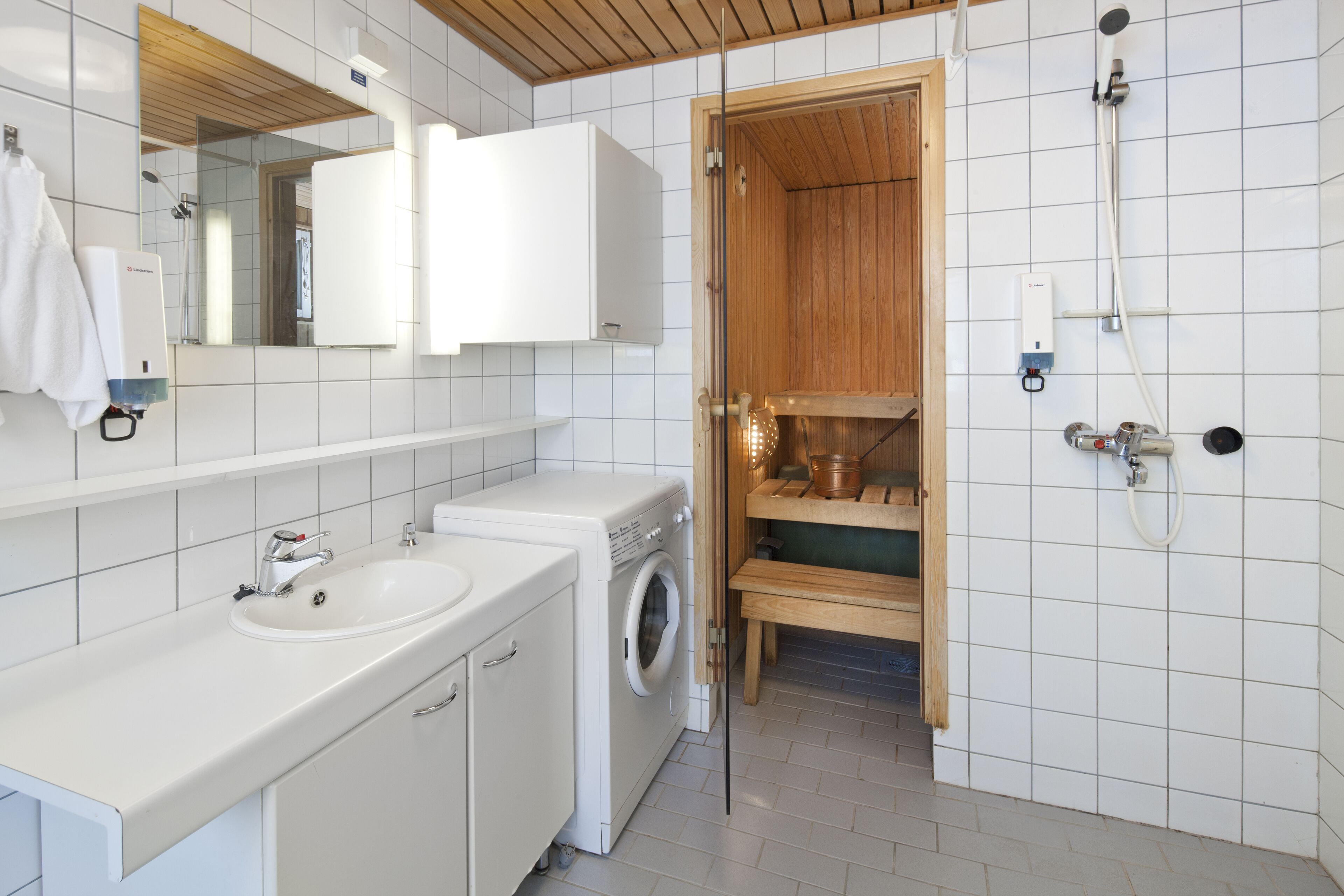 A modern bathroom with a white sink, a washing machine, a wooden shower enclosure, and a mirror above the sink.
