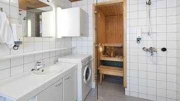 A modern bathroom with a white sink, a washing machine, a wooden shower enclosure, and a mirror above the sink.