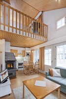 A spacious living area with a high ceiling, a fireplace, a dining area, and a sofa.