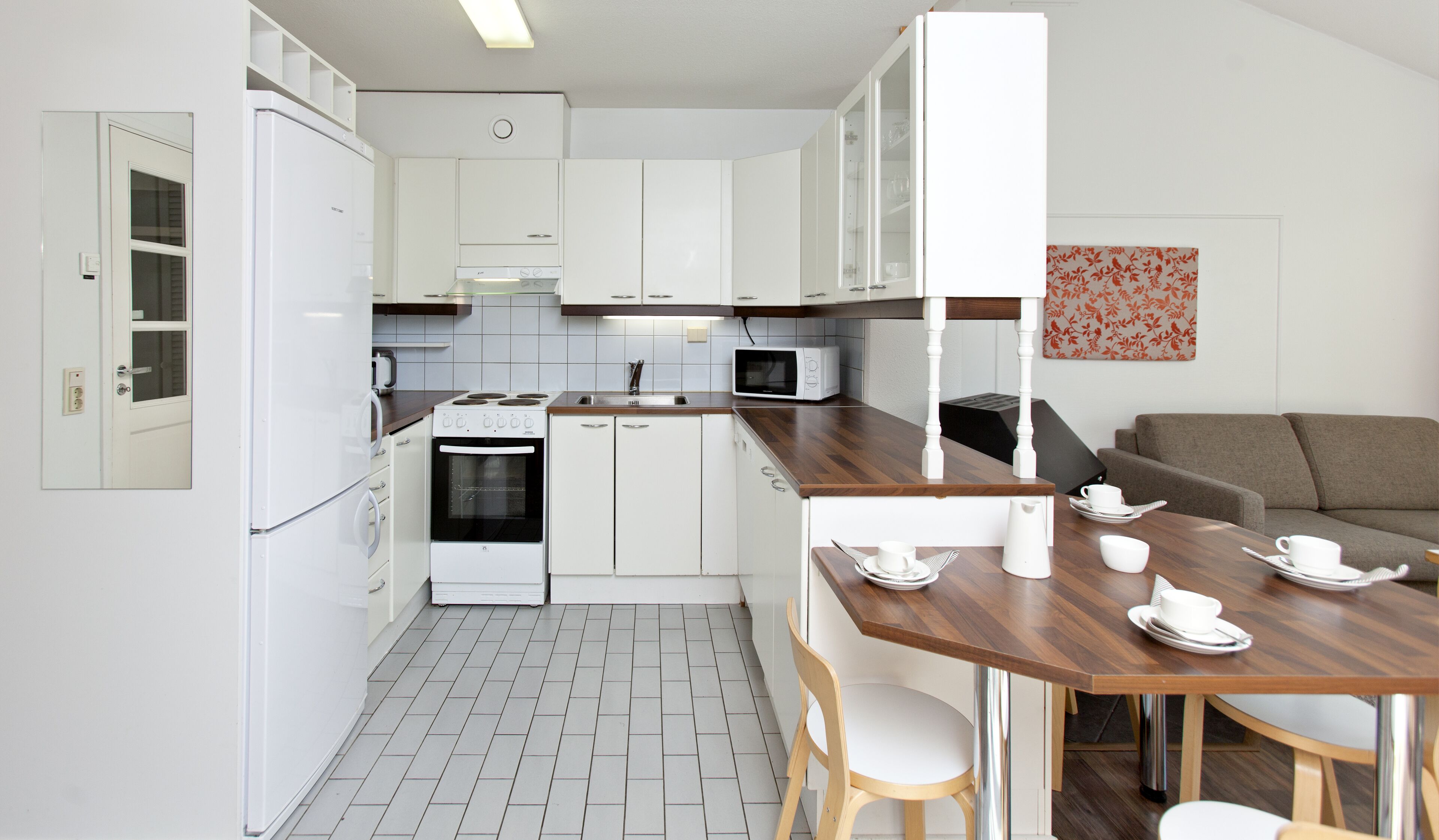A compact kitchen with white appliances, a dining area with a wooden table and chairs, and a sofa.