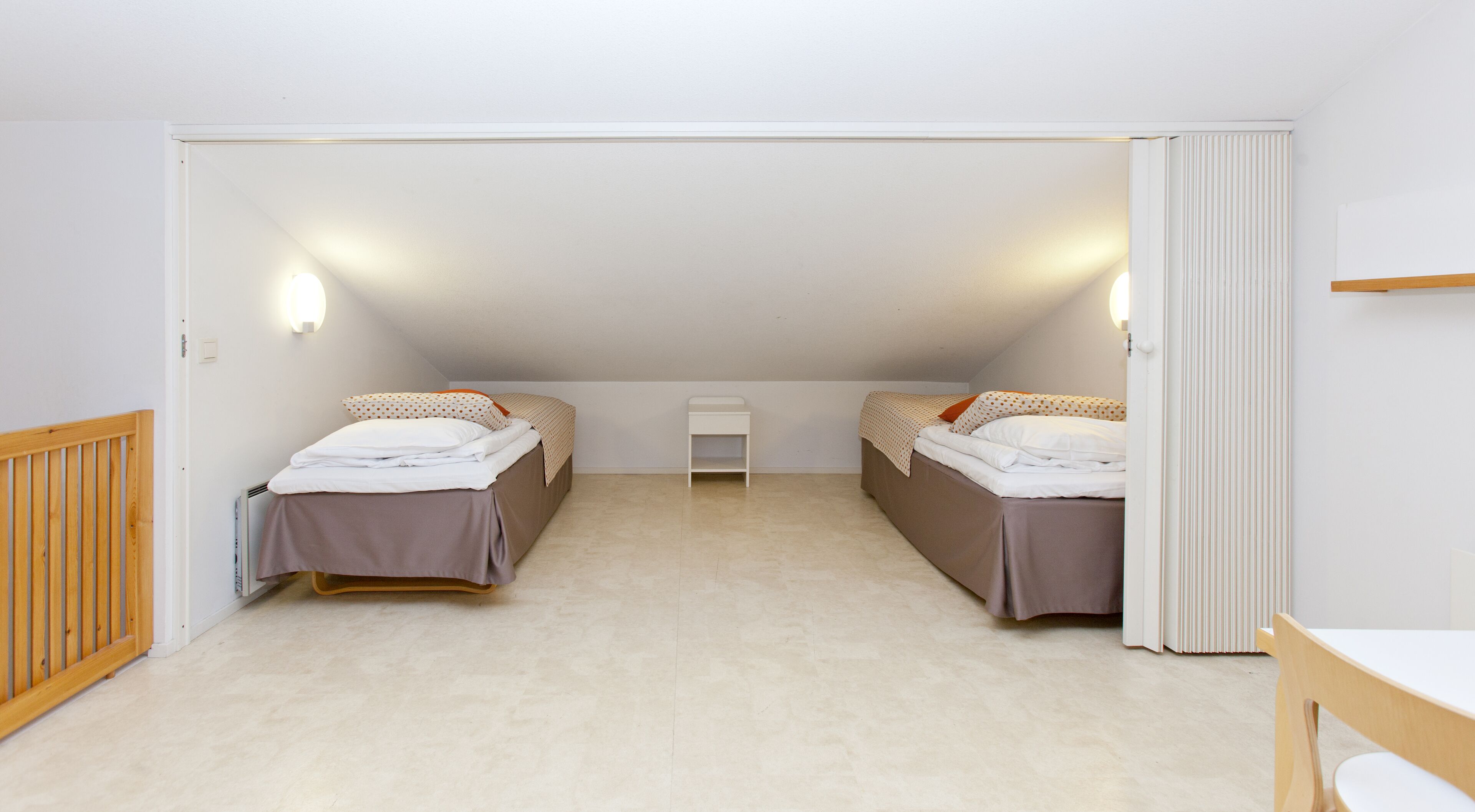 A small, well-lit attic bedroom with two beds, a small table, and a radiator.