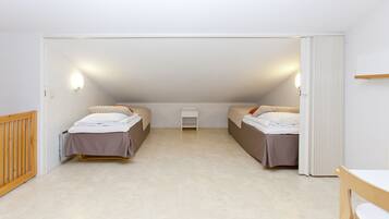 A small, well-lit attic bedroom with two beds, a small table, and a radiator.