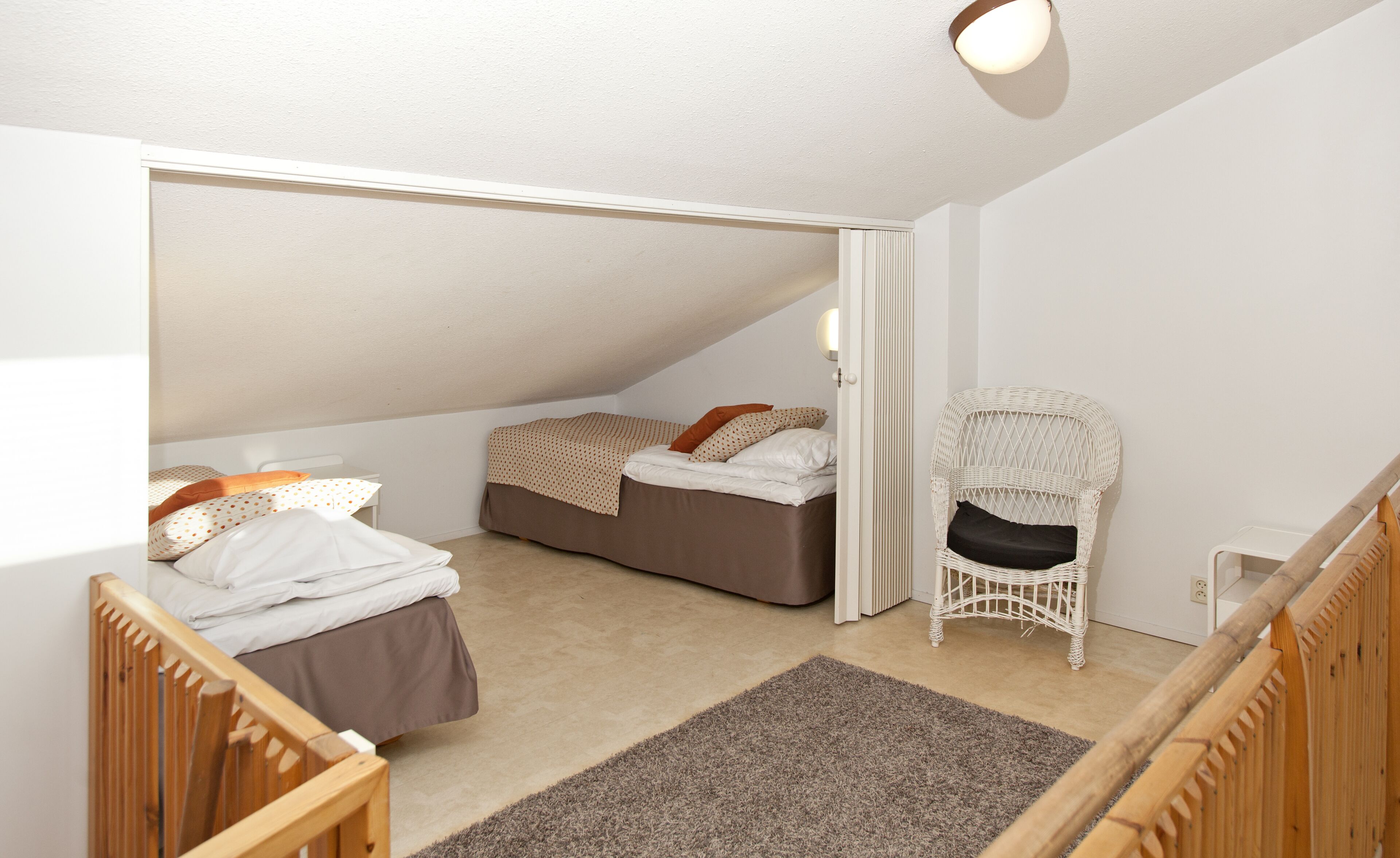 A small, well-lit room with two beds, a white wicker chair, and a wooden crib.