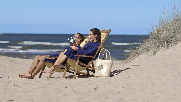 Deux personnes sont assises sur des chaises de plage, sur une plage de sable, avec l’océan en arrière-plan.
