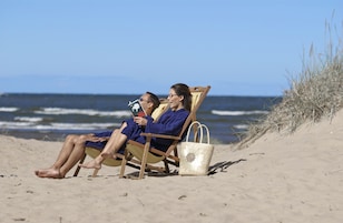 Two people sitting on beach chairs on a sandy beach with the ocean in the background.