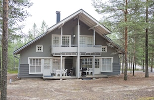 A two-story cabin with a balcony, surrounded by trees.