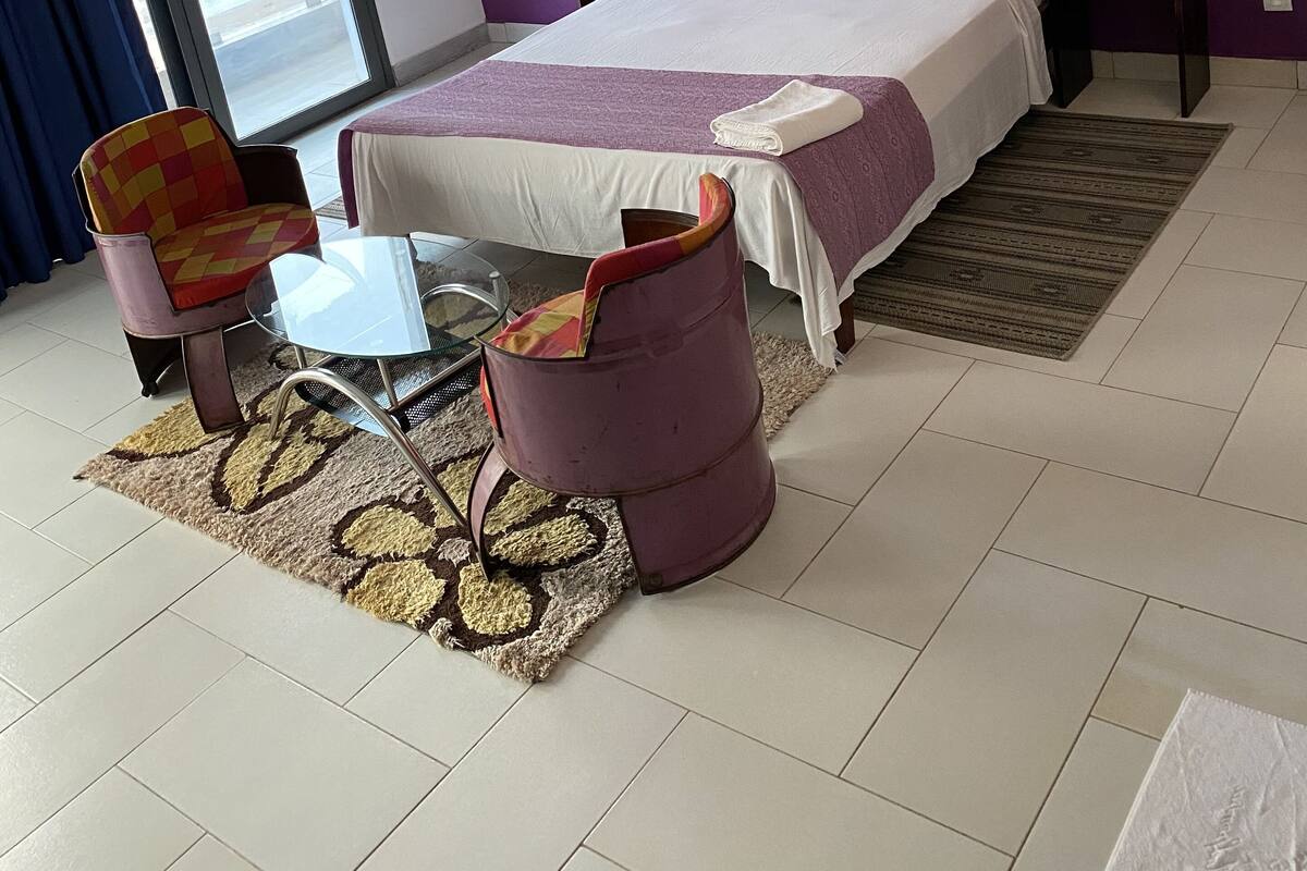 A modern bedroom with a large bed, purple walls, a window with a view, a small table, and a chair.