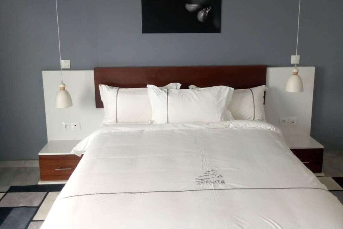 A modern bedroom with a large bed, white bedding, and a headboard with pendant lights.