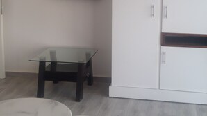 Huoneessa on seinälle asennettu taulutelevisio, valkoinen vaatekaappi sekä kaksi pyöreää pöytää, joiden jalat ovat mustat.