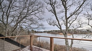 Eine Holzterrasse mit Metallgeländer, das auf einen See blickt, umgeben von entlaubten Bäumen.
