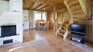 Interior de madera con chimenea, comedor y televisor sobre un soporte.