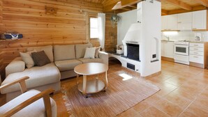 Interior acogedor de una cabaña con sofá, una mesita redonda, chimenea y zona de cocina.