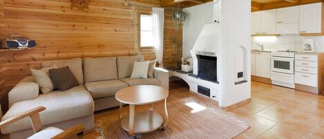 Ein gemütliches Blockhaus-Interieur mit einer Couch, einem kleinen runden Tisch, einem Kamin und einer Küchenzeile.