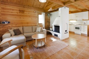 Interior acogedor de una cabaña con sofá, una mesita redonda, chimenea y zona de cocina.
