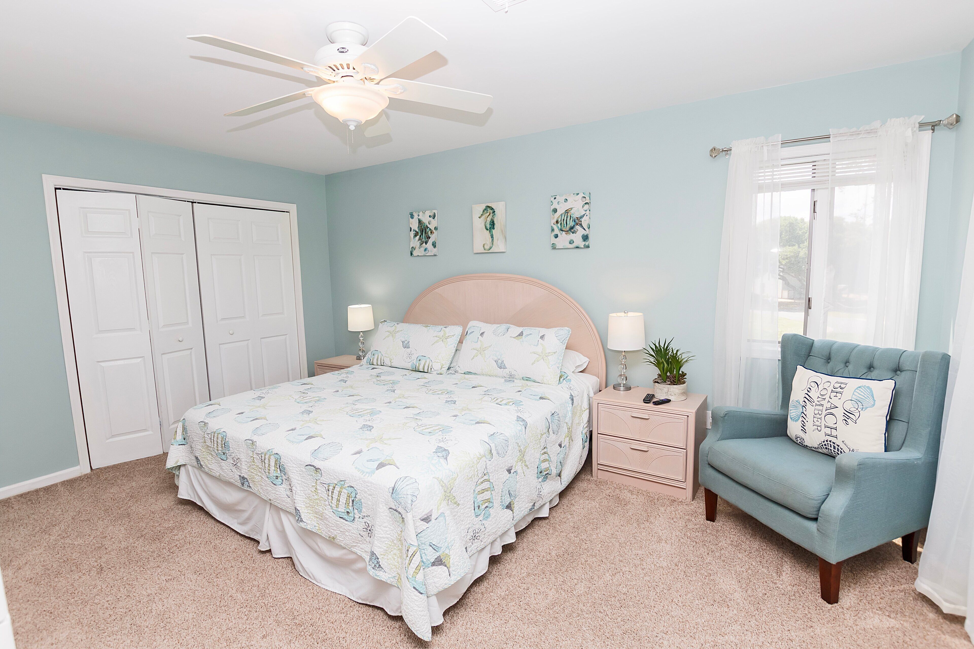 A bedroom with a bed, a chair, a nightstand, and a ceiling fan.