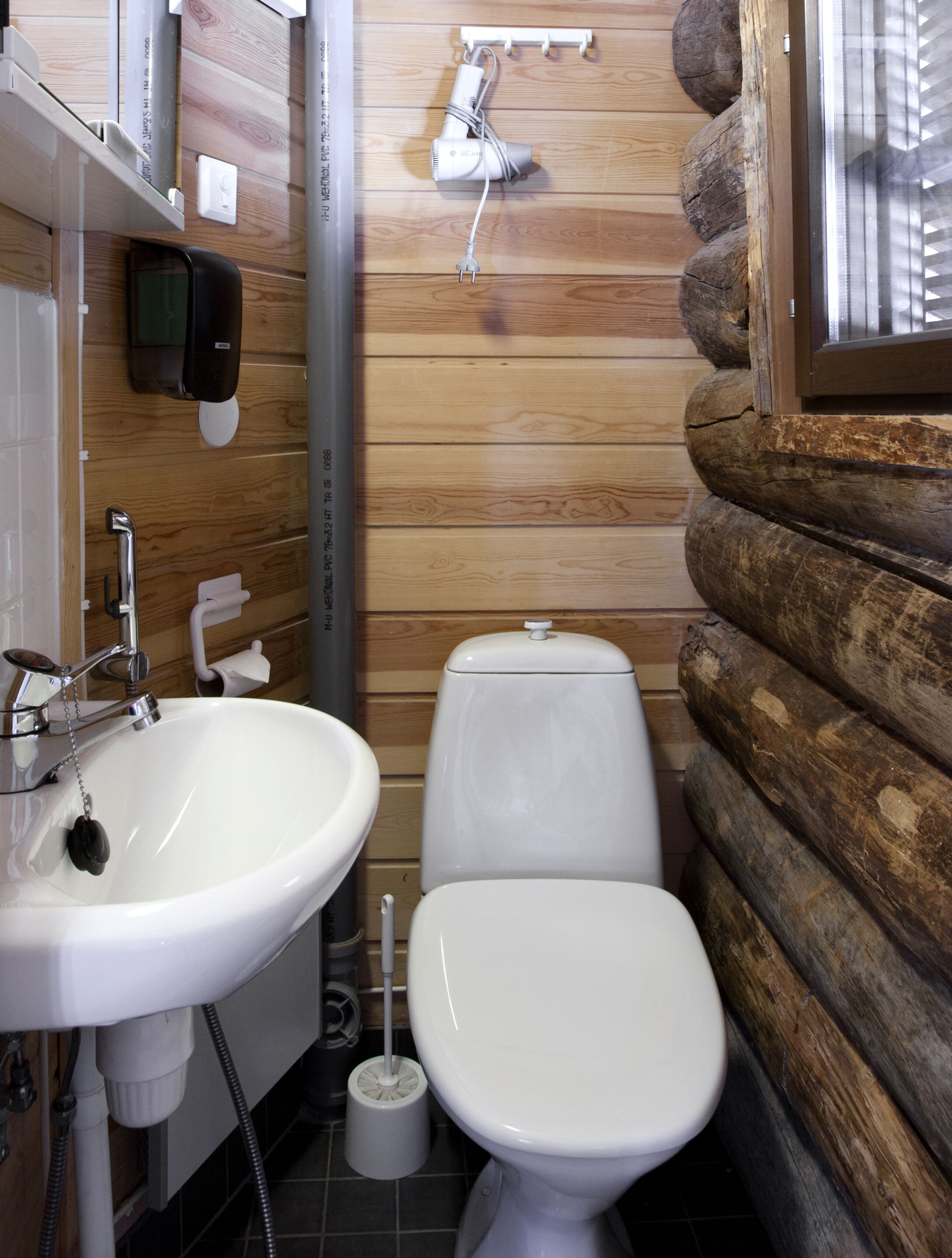 Une petite salle de bain avec un lavabo blanc, des toilettes et une douchette portative fixée au mur.