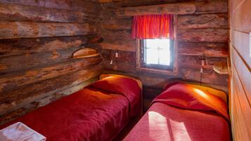 Une cabane avec deux lits en bois, une fenêtre ornée d’un rideau rouge et un mur en bois.