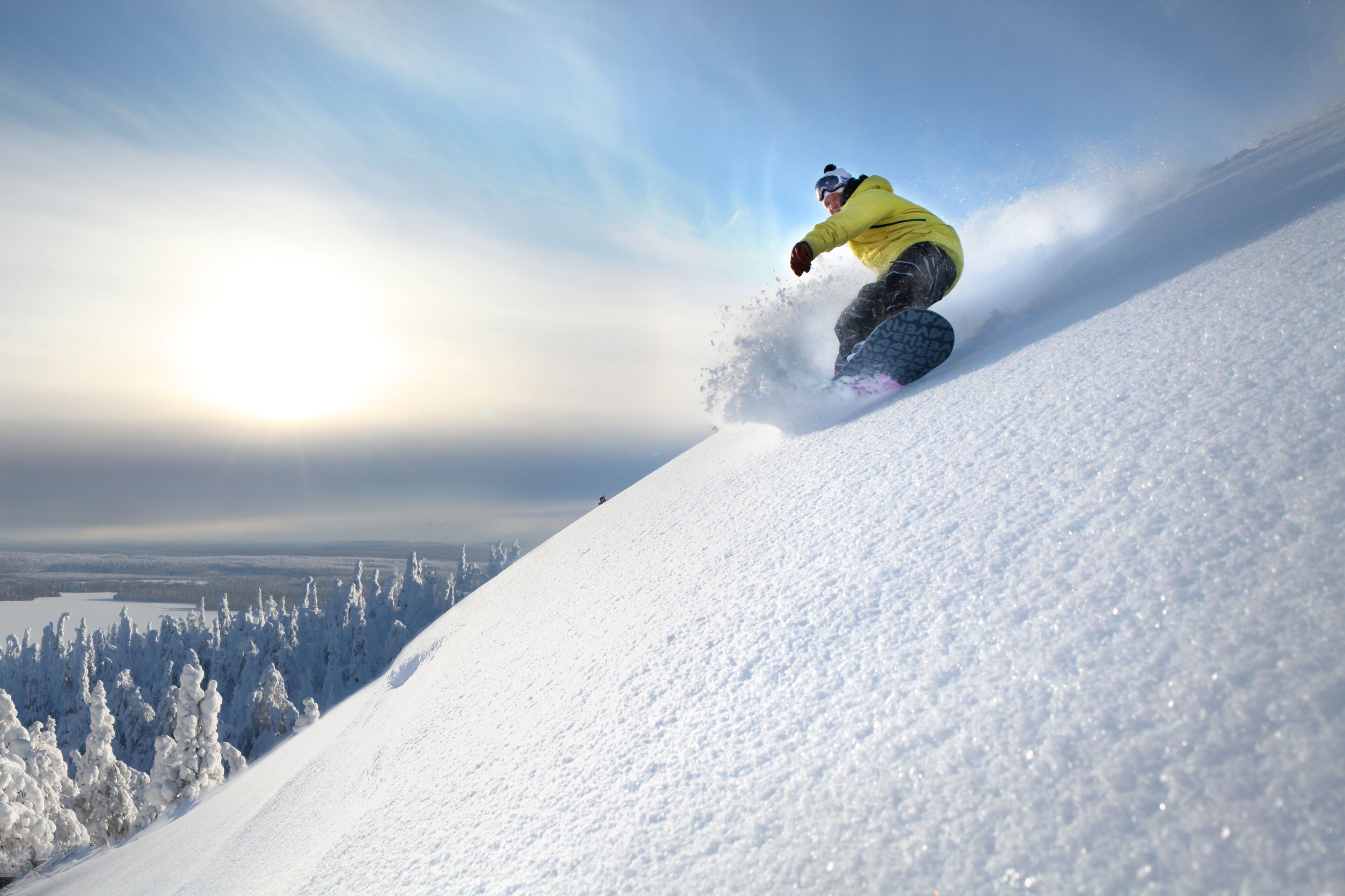 Un snowboardeur sur une pente enneigée, sous un ciel dégagé, avec un paysage lointain.