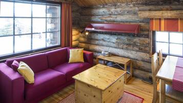 A log cabin interior with a red sofa, wooden coffee table, and a dining table with a red tablecloth.