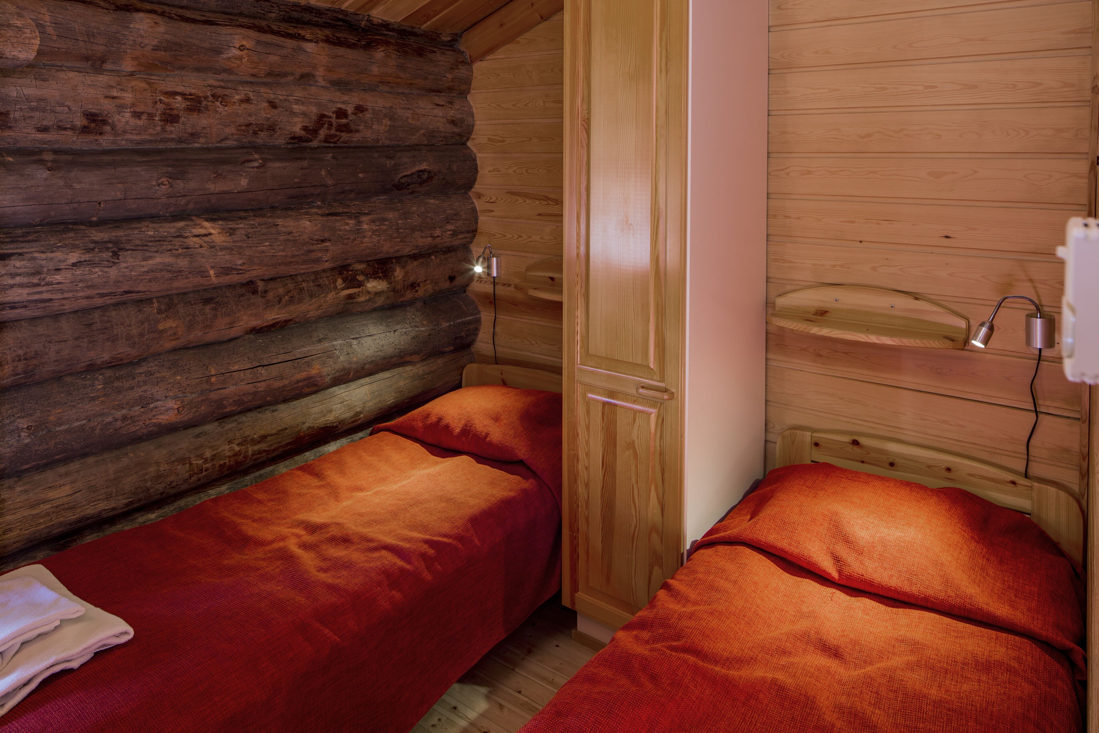 A cabin-style room with two single beds, wooden walls, and a small wooden shelf.