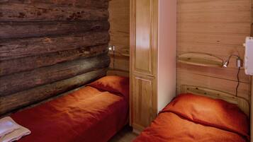 A cabin-style room with two single beds, wooden walls, and a small wooden shelf.
