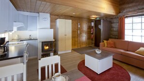 Hyggelig hytteinteriør med tekøkken, pejs, sofa og spiseplads.