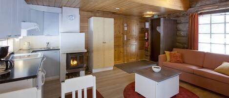 A cozy cabin interior with a kitchenette, a fireplace, a sofa, and a dining area.