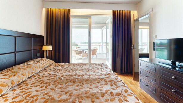 A hotel room with a bed, a TV, a dresser, and a balcony with a table and chairs. - Holiday Club Naantali Apartments (Naantali)