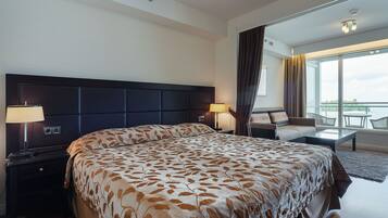 Habitación de hotel con una cama grande, dos mesitas de noche con lámparas, un sofá y un balcón con vistas.