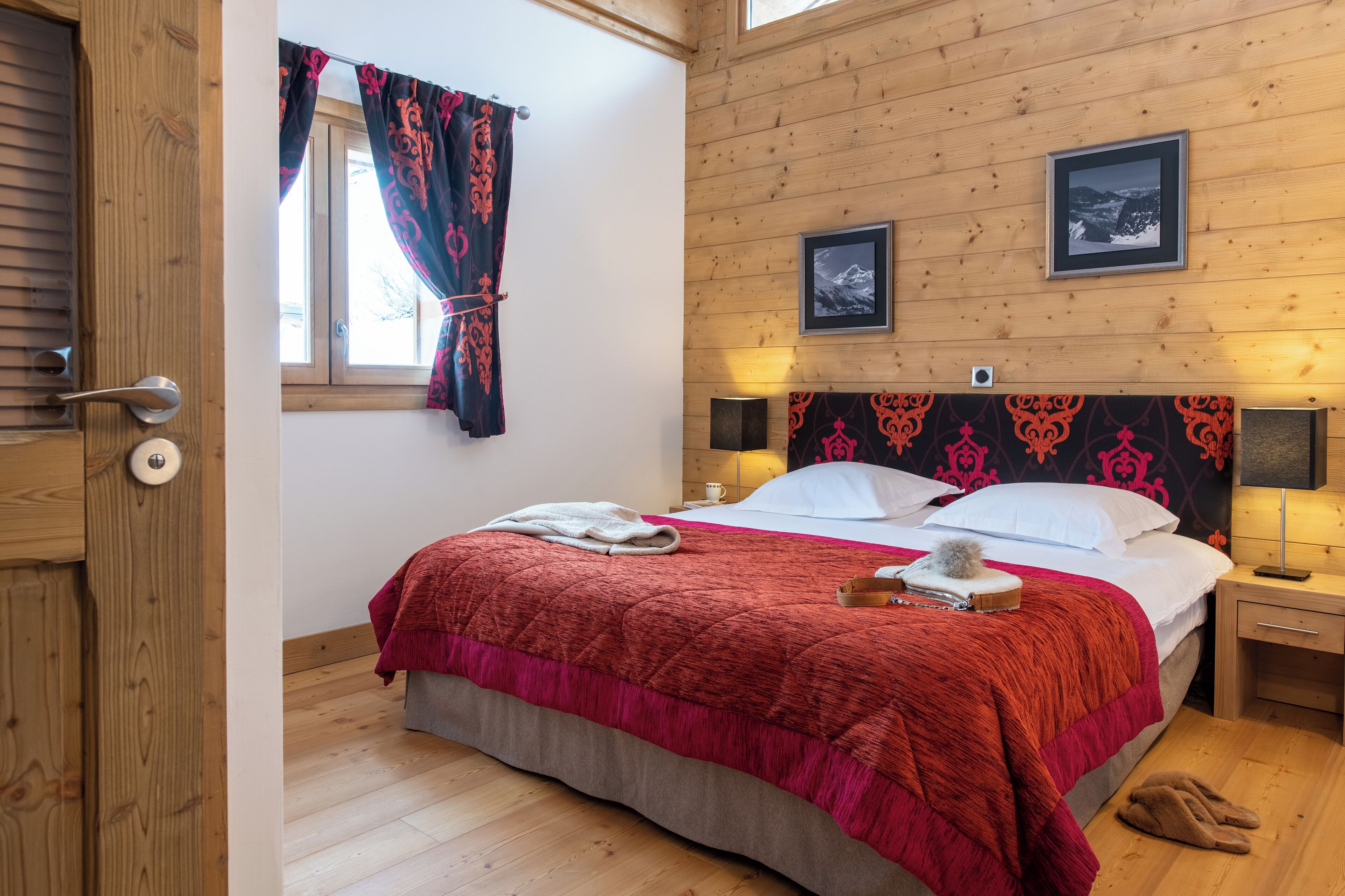 A wooden-paneled room with a bed, a window with curtains, and two framed pictures on the wall.