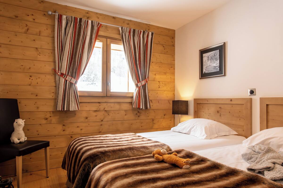Une pièce aux murs lambrés, contenant un lit, une chaise, une lampe et un jouet en peluche.