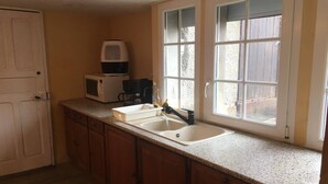 A kitchen with a double sink, a microwave, a coffee maker, and a window with a view of the outside.