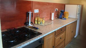 A kitchen with a gas stove, wooden cabinets, a white refrigerator, and various kitchen utensils and appliances on the countertop.